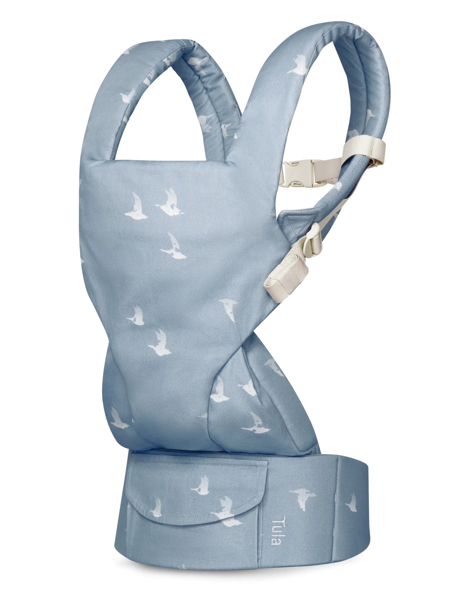 A light blue cotton baby carrier with a white bird pattern, shown on a plain white background. The brand name 'Tula' is visible on the front waist belt.