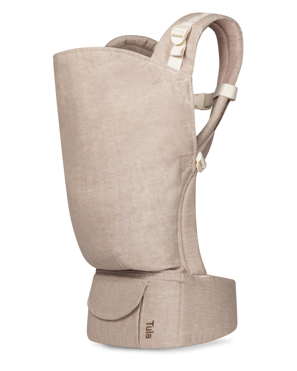 A beige textured toddler carrier shown from the side against a plain white background, featuring adjustable straps and a small 'Tula' brand label on the waistband.
