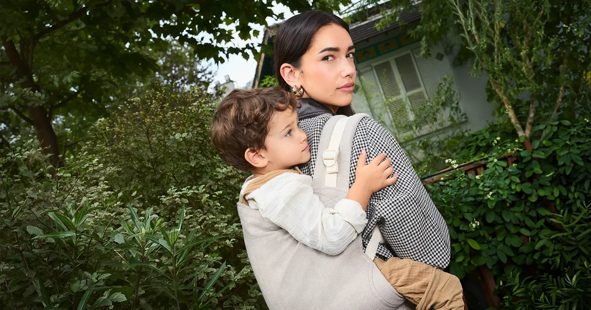 Woman carrying her 3 year old toddler in the Tula Kid toddler carrier in linen herringbone sand