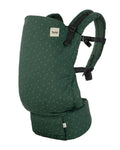 A green toddler carrier with a subtle repeating pattern, featuring black adjustable shoulder straps and a white 'tula' brand label on the front.
