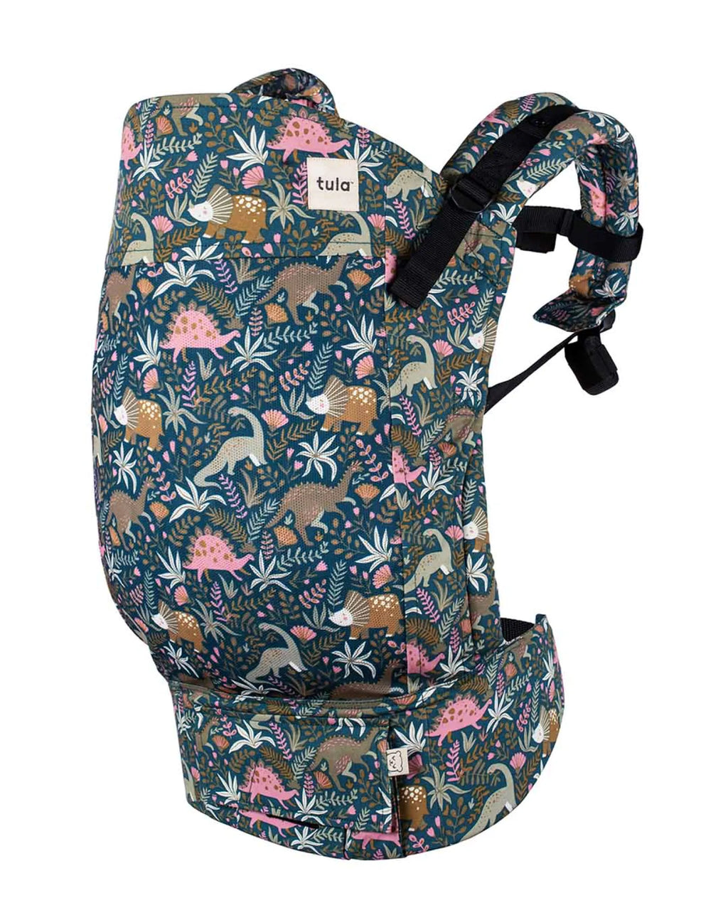 A baby carrier by Tula featuring a detailed prehistoric dinosaur and fern pattern on a dark teal background, with black adjustable shoulder straps and a front mesh pocket.