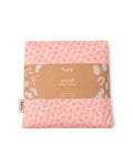 A folded Tula baby carrier wrap in a light pink color with a small orange floral pattern, wrapped in a brown kraft paper band with white text and illustrations, on a plain white background.